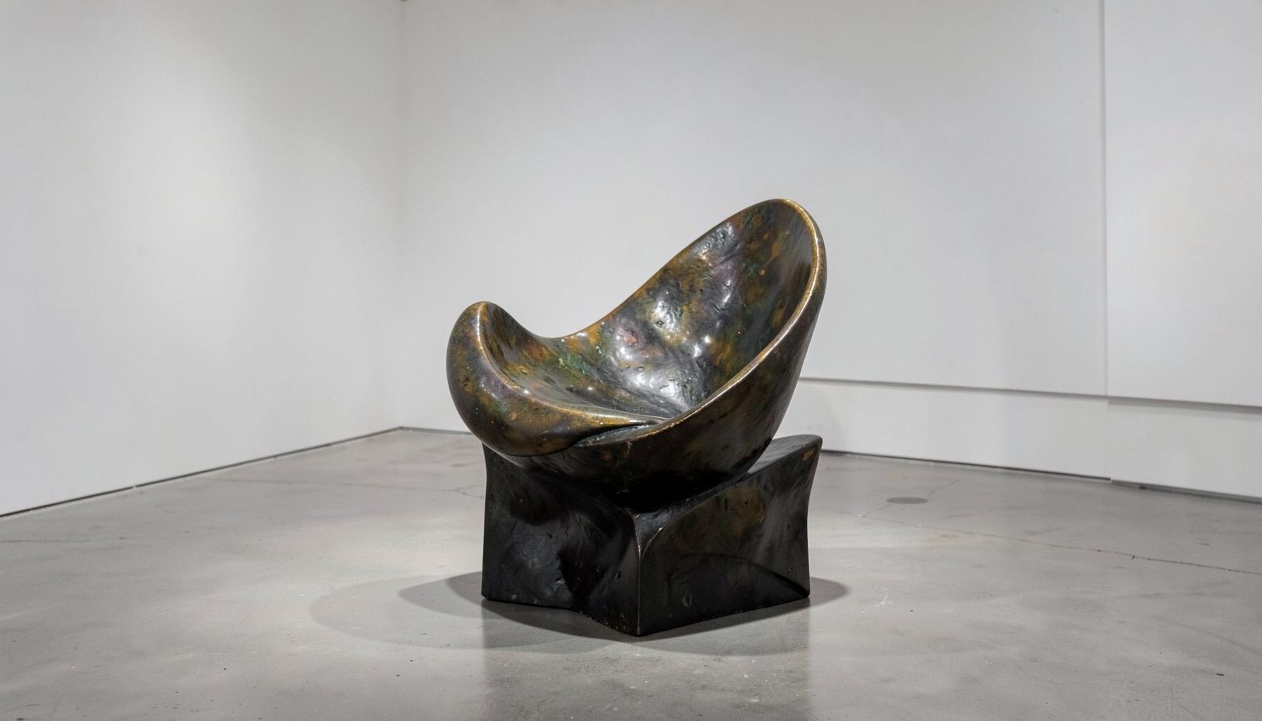 A sculptural bronze chair with sweeping asymmetrical curves in a gallery setting